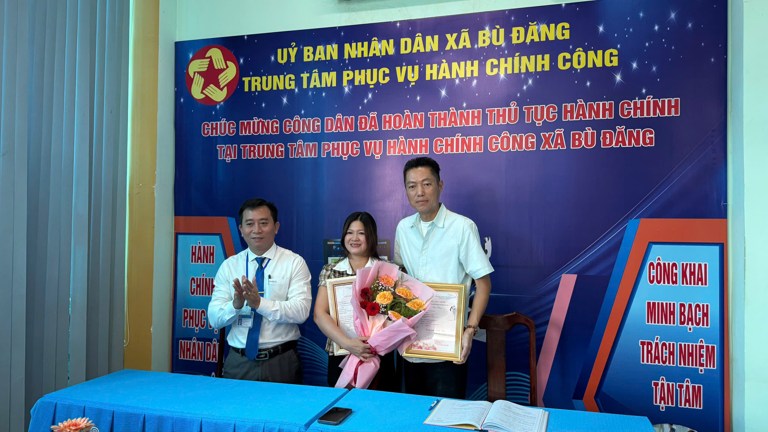 Đồng chí Nguyễn Cảnh Thảo - Phó Chủ tịch UBND xã Bù Đăng (bìa trái) trao Giấy chứng nhận đăng ký kết hôn, thư chúc mừng và hoa cho đôi bạn trẻ: Nguyễn Paul vinh và Nguyễn Thị Thanh Thủy